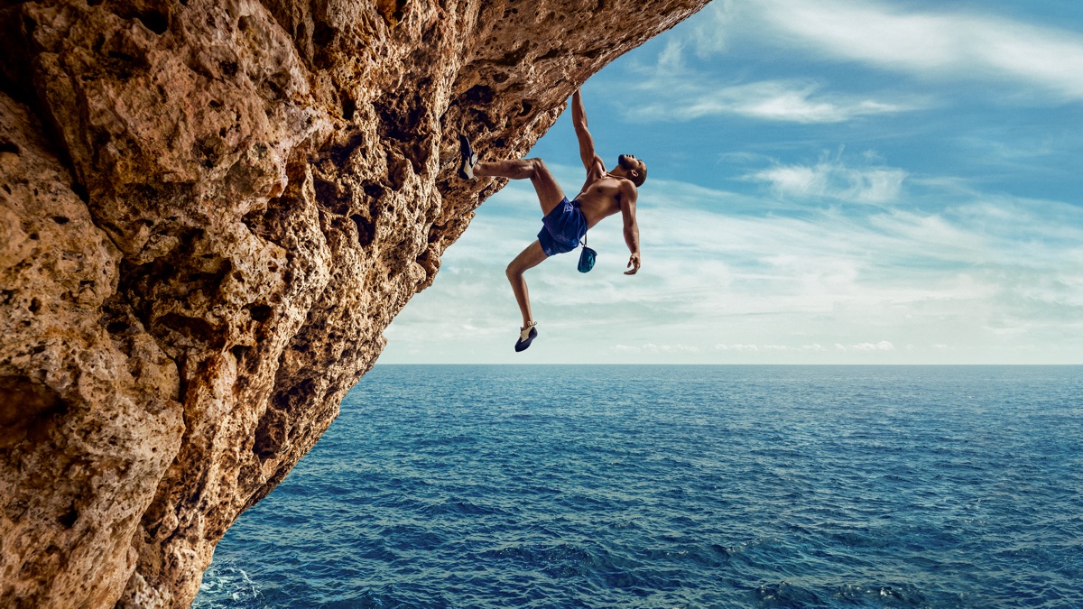A climber scaling a sheer rock face in a dramatic outdoor setting, seen in Apple Immersive Video
