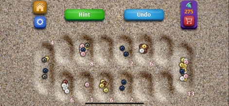 Mancala. - Disfruta de un sereno escenario playero, donde la textura de arena y las piedras pulidas de diversos colores crean un entorno de juego orgánico y visualmente agradable.