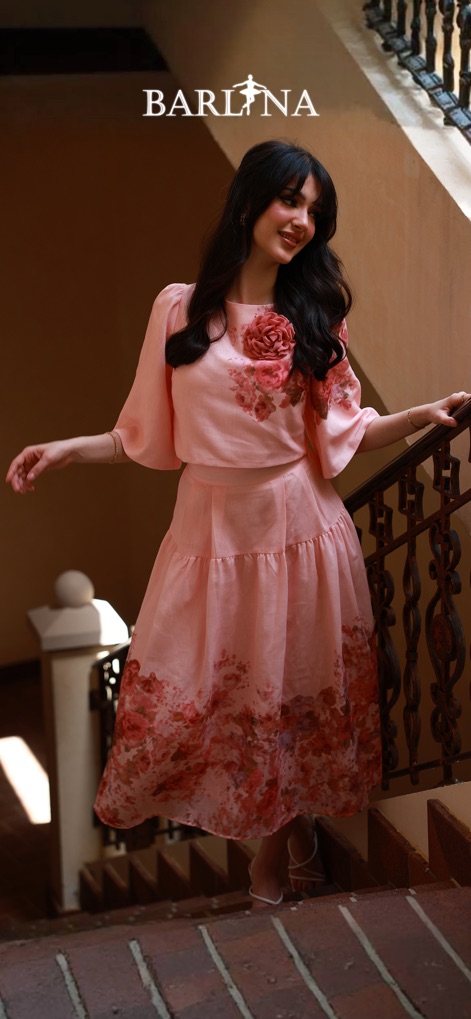 بارلينا | Barlina - Esta imagem destaca a sofisticação das coleções, exibindo um vestido floral rosa com mangas bufantes e uma saia com estampa floral na barra.