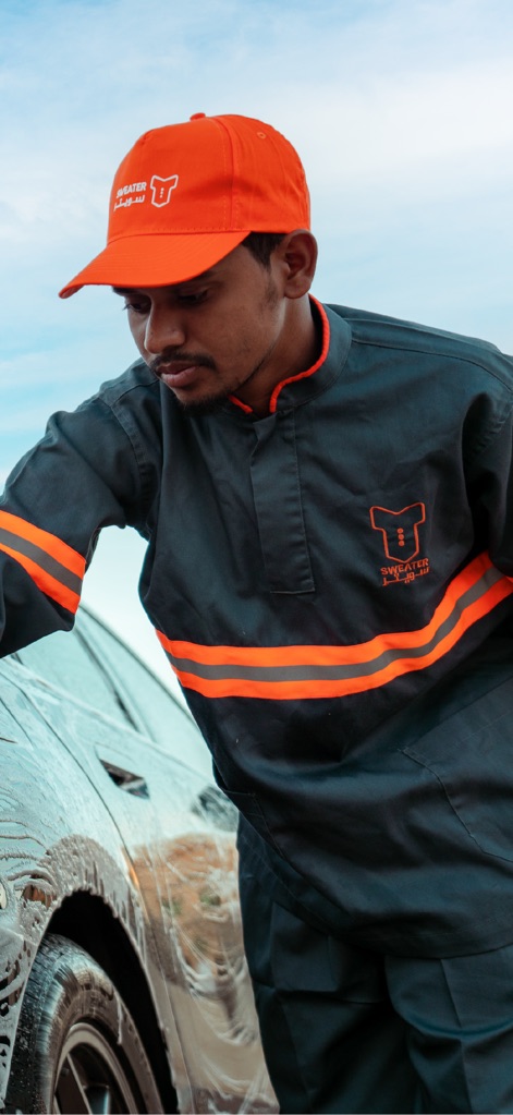 Sweater | Car Wash - O profissional, vestindo o uniforme com o "Sweater logo" e concentrado na limpeza da roda do carro, enfatiza a atenção aos detalhes e a qualidade da execução do serviço.